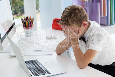 Businessman covering eyes while sitting with laptop at desk