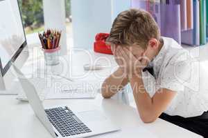 Businessman covering eyes while sitting with laptop at desk