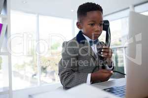 Businessman using telephone while looking at laptop