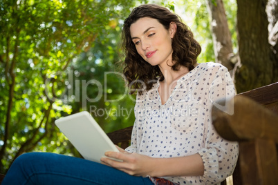 Woman sitting on bench and using digital tablet in garden on a sunny day