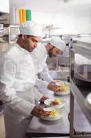 Two chefs garnishing food in commercial kitchen
