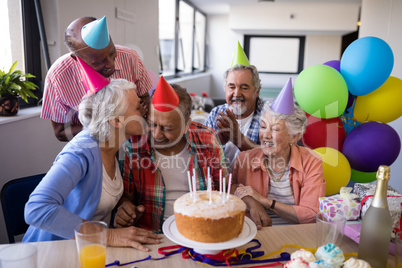 Friend kissing senior man while celebrating at party