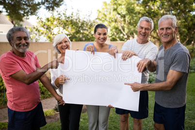 Portrait of smiling senior people with trainer holding blank placard