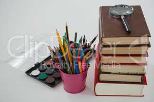 Book stack, magnifying glass, color pencils and palette on white background