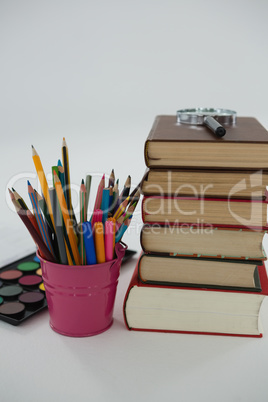 Book stack, magnifying glass, color pencils and palette on white background