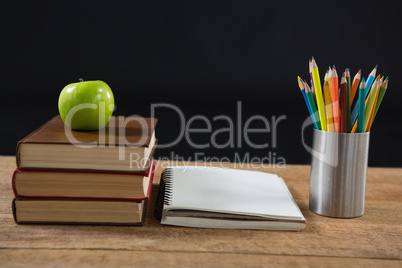 Apple on book stack with color pencils on table