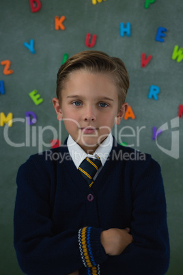 Schoolboy standing with arms crossed against chalkboard