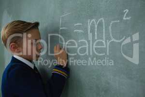 Schoolboy writing maths formula on chalkboard