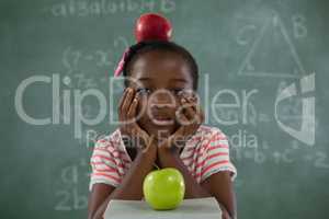 Schoolgirl sitting with red apple on her head against chalkboard
