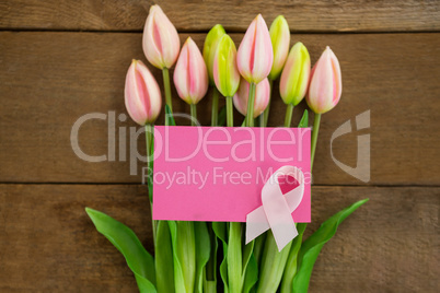 Overhead view of pink Breast Cancer Awareness ribbon with blank card on tulips
