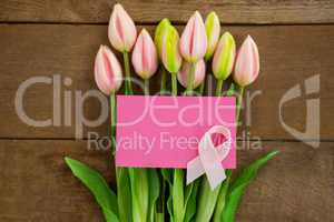 Overhead view of pink Breast Cancer Awareness ribbon with blank card on tulips