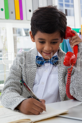 Smiling businessman writing while talking on land line phone