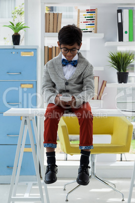 Full length of businessman using smart phone while sitting on desk