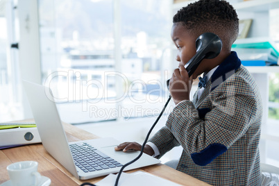 Serious businessman using telephone and laptop at desk