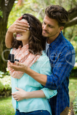 Happy man covering woman eyes while gifting her ring