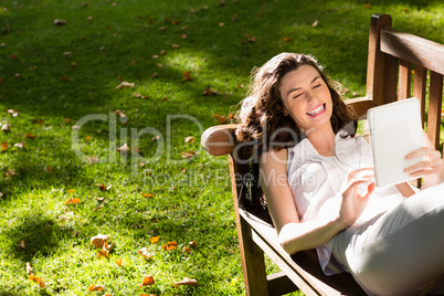 Woman lying on bench and using digital tablet in garden on a sunny day
