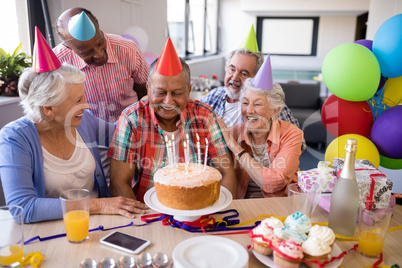 Cheerful friends looking at senior man in birthday party