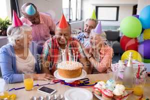 Cheerful friends looking at senior man in birthday party