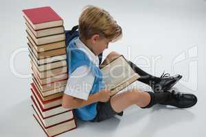 Schoolboy reading book while sitting against books stack