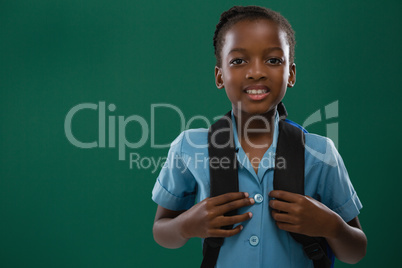 School girl with backpack standing against chalk board