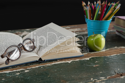 Spectacles on open book with pen holder and apple
