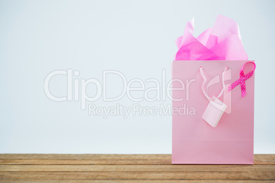 Pink Breast Cancer Awareness ribbon on shopping bag over wooden table
