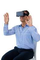 Smiling businessman with vr glasses gesturing while sitting on chair