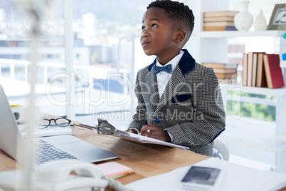 Thoughtful businessman with clipboard sitting at desk