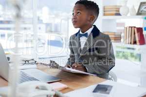Thoughtful businessman with clipboard sitting at desk