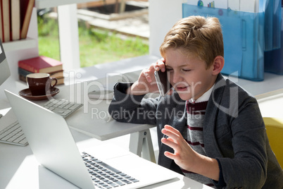 Businessman gesturing wile talking on mobile phone by laptop  at desk