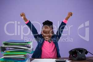 Portrait of happy businesswoman with arms raised at desk