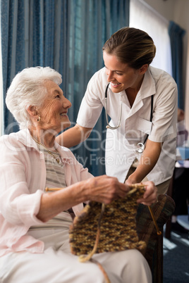 Smiling senior woman knitting while looking at female doctor