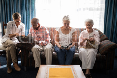 Smiling female doctor reading book by senior people sitting on sofa against window