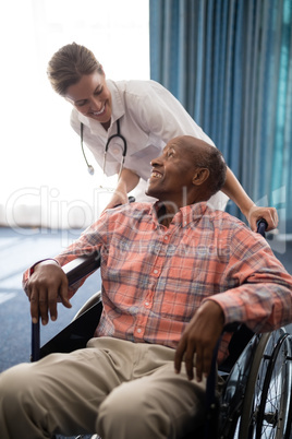 Smiling female doctor looking at disabled senior man sitting on wheelchair against window