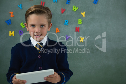 Schoolboy holding digital tablet against chalkboard