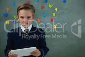 Schoolboy holding digital tablet against chalkboard