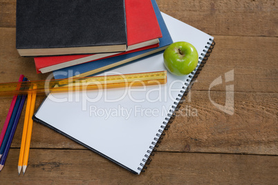 Green apple and school supplies on wooden table