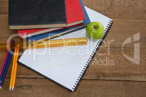 Green apple and school supplies on wooden table