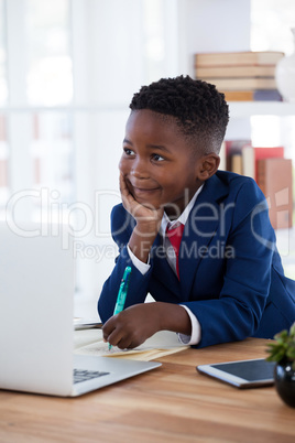 Thoughtful businessman with hand on chin looking away while writing n paper