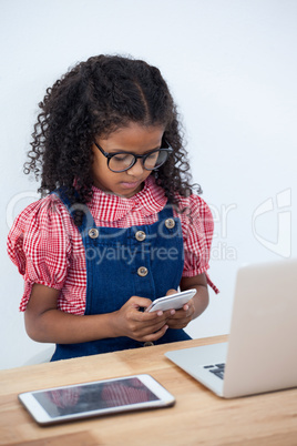 Businesswoman wearing eyeglasses using phone while sitting by laptop