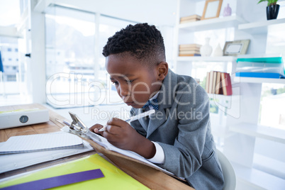 Boy imiting as businessman writing on paper attached to clipboard