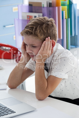 Thoughtful businessman with head in hands by laptop at desk