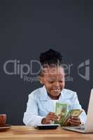 Businesswoman counting paper currency while using laptop