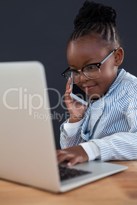 Confident smiling businesswoman using phone while working on laptop