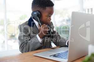 Businessman with laptop talking on telephone at desk