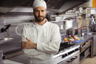 Portrait of confident chef standing with arms crossed in commercial kitchen