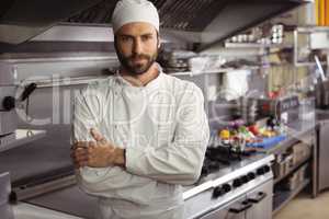 Portrait of confident chef standing with arms crossed in commercial kitchen
