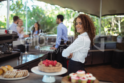 Portrait of smiling waitress standing with arms crossed at counter