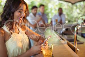 Smiling woman using mobile phone while having a glass of beer