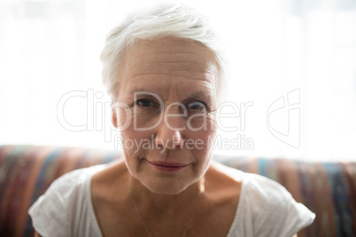 Close-up portrait of senior woman sitting on sofa against window